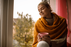 woman in fall sitting next to window with coffee