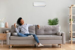 What Indoor Air Quality Accessories Can Help Keep Me Healthy? Image shows woman sitting on a grey couch and looking relaxed.